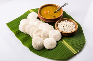 traditional south indian food or recipe idli or idly with sambar or sambhar and coconut chutney in earthen bowl over green banana leaf on white background clipart