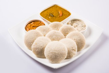 traditional south indian food, idli or idly with sambar and white coconut chutney and red chutney in white ceramic square plate and bowl on white background, front view isolated on white background clipart