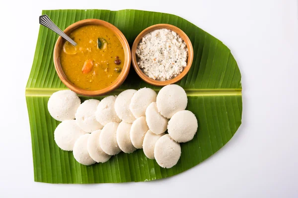 Traditionelles südindisches Essen oder Rezept idli oder untätig mit Sambar oder Sambhar und Kokosnuss-Chutney in irdener Schüssel über grünem Bananenblatt auf weißem Hintergrund — Stockfoto