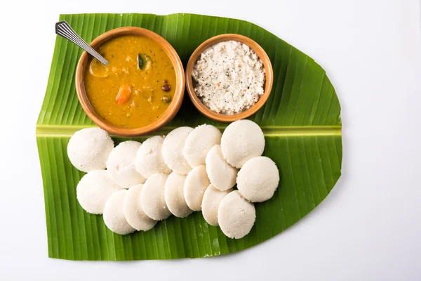 traditional south indian food or recipe idli or idly with sambar or sambhar and coconut chutney in earthen bowl over green banana leaf on white background