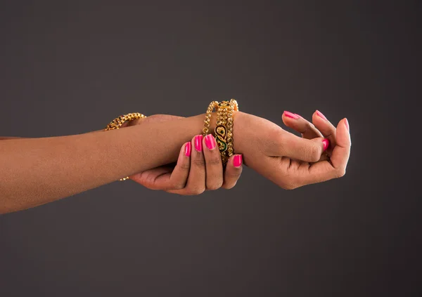 Arany karperecek a kezében, kecses jelent a lányok kézzel visel arany karperecek, Designer arany karperecek és kézi, lányok kezek arany karperecek, closeup, elszigetelt szürke háttér — Stock Fotó