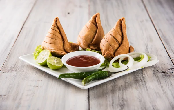 Indiai híres snack élelmiszer samosa egy tányérra citrommal, hagymával és zöld sült chilipaprika — Stock Fotó