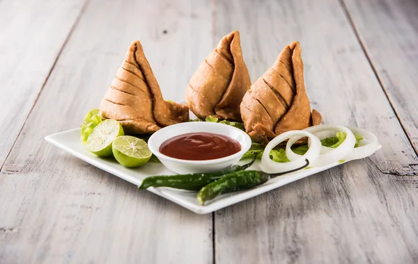 Indické proslulé občerstvení Samosa na talíři s citronem, cibulí a zeleným smaženým chilli papričkami — Stock fotografie