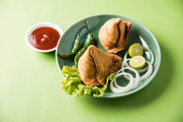 Comida india famosa merienda Samosa en un plato con limón, cebolla y chile frito verde —  Fotos de Stock