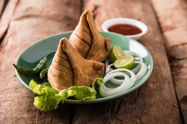 Comida de refeição leve famosa indiana Samosa em um prato com limão, cebola e pimenta frita verde — Fotografia de Stock