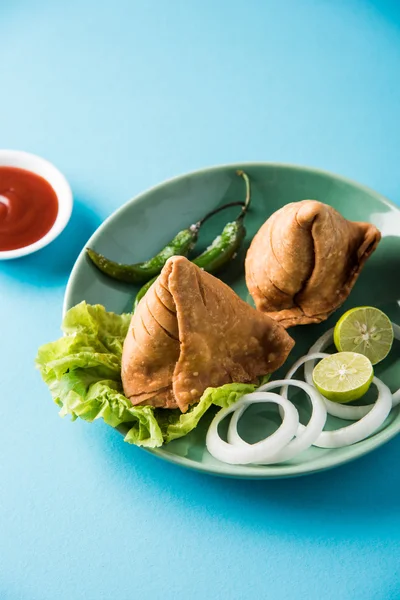 Indické proslulé občerstvení Samosa na talíři s citronem, cibulí a zeleným smaženým chilli papričkami — Stock fotografie