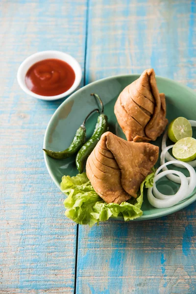 Ινδικό διάσημο σνακ φαγητό samosa σε ένα πιάτο με λεμόνι, κρεμμύδι και πράσινο τηγανητό τσίλι — Φωτογραφία Αρχείου