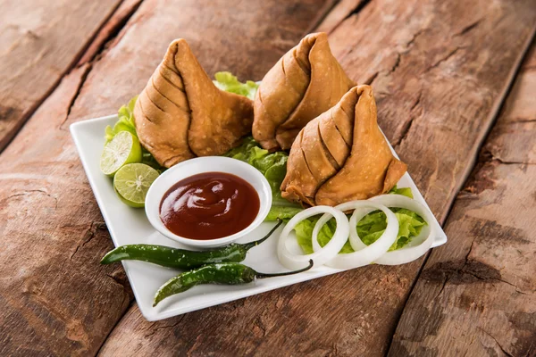 Comida de refeição leve famosa indiana Samosa em um prato com limão, cebola e pimenta frita verde — Fotografia de Stock