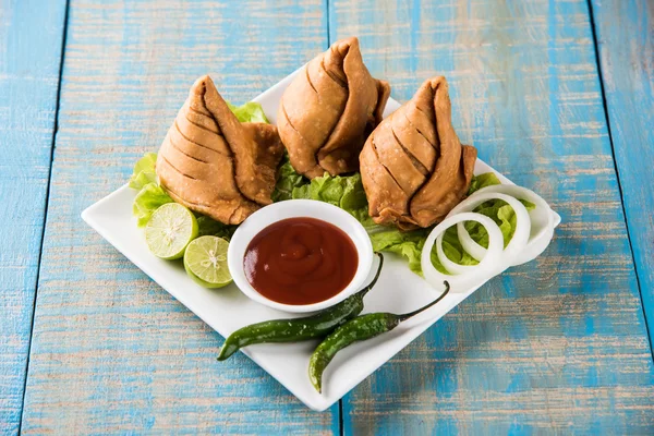 Comida india famosa merienda Samosa en un plato con limón, cebolla y chile frito verde —  Fotos de Stock