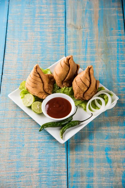 Indian famous snack food Samosa on a plate with lemon, onion and green fried chilli — Stock Photo, Image