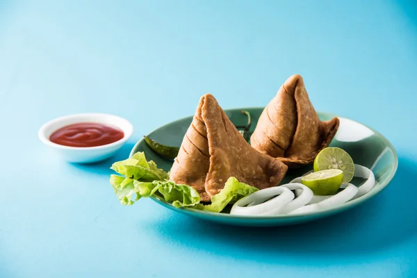 Comida de refeição leve famosa indiana Samosa em um prato com limão, cebola e pimenta frita verde — Fotografia de Stock