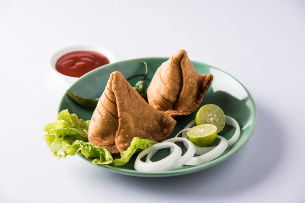 Comida de refeição leve famosa indiana Samosa em um prato com limão, cebola e pimenta frita verde — Fotografia de Stock