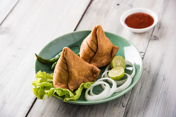 Comida de refeição leve famosa indiana Samosa em um prato com limão, cebola e pimenta frita verde — Fotografia de Stock