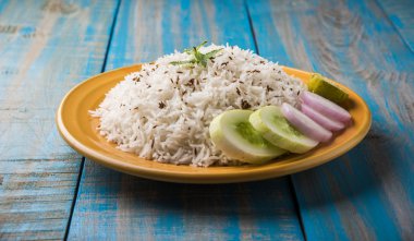 Jeera pirinç, uzun taneli basmati kızarmış Kimyon tohumu, sarı bir seramik tabak içinde yeşil salata ile servis ile aromalı pirinç pişmiş