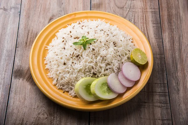 Джера рис, длиннозернистый приготовленный рис басмати с ароматом жареного тмина, подается в желтой керамической тарелке с зеленым салатом — стоковое фото