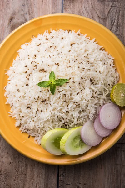 Orez jeera, orez basmati gătit cu cereale lungi, aromat cu semințe de chimen prăjit, servit într-o placă ceramică galbenă cu salată verde — Fotografie, imagine de stoc