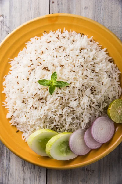 Orez jeera, orez basmati gătit cu cereale lungi, aromat cu semințe de chimen prăjit, servit într-o placă ceramică galbenă cu salată verde — Fotografie, imagine de stoc