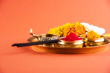 Beautifully Decorated Pooja Thali for diwali celebration to worship, huldi or turmeric powder and kumkum, flowers, scented sticks in brass plate on orange background, hindu puja thali clipart