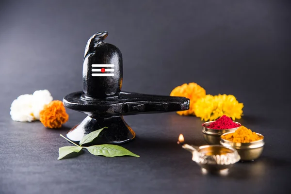 Shiva Linga compuesta de piedra negra decorada con flores y hoja de bael conocida como Aegle marmelos, sobre fondo negro, maha shiva ratri un festival de Dios hindú shankar o shankar bhagwan o bholenath — Foto de Stock