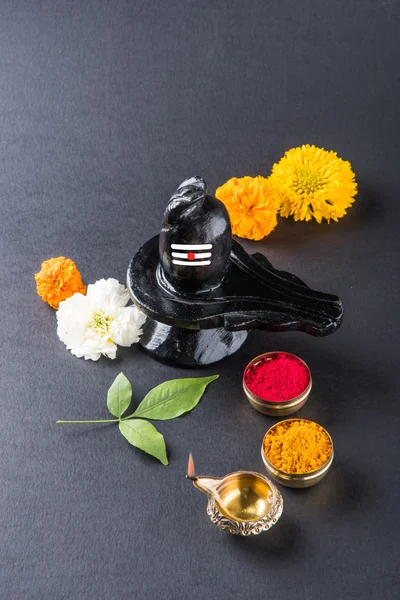 Shiva Linga composta de pedra preta decorada com flores e folha de bael conhecido como Aegle marmelos, sobre fundo preto, maha shiva ratri um festival de hindu Deus shankar ou shankar bhagwan ou bholenath — Fotografia de Stock