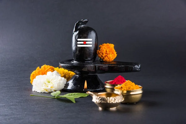 Shiva Linga composta de pedra preta decorada com flores e folha de bael conhecido como Aegle marmelos, sobre fundo preto, maha shiva ratri um festival de hindu Deus shankar ou shankar bhagwan ou bholenath — Fotografia de Stock