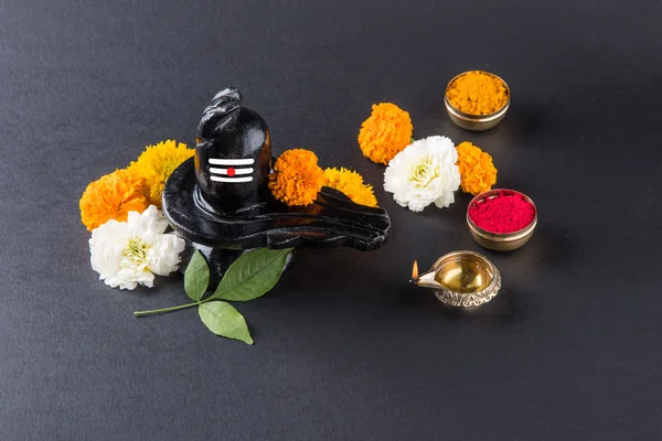 Shiva Linga compuesta de piedra negra decorada con flores y hoja de bael conocida como Aegle marmelos, sobre fondo negro, maha shiva ratri un festival de Dios hindú shankar o shankar bhagwan o bholenath —  Fotos de Stock