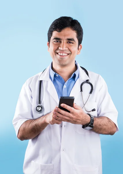 Porträtt av säker indiska manliga läkare visar smarta telefonen över blå bakgrund. indisk läkare med smart telefon, asiatiska läkare pekar smart telefon — Stockfoto