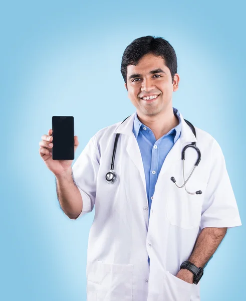 Retrato de médico indiano confiante mostrando telefone inteligente sobre fundo azul. indiana médico com inteligente telefone, asiático médico apontando inteligente telefone — Fotografia de Stock