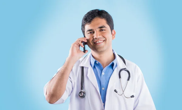 Retrato del médico indio confiado que muestra el teléfono inteligente sobre fondo azul. médico indio con teléfono inteligente, médico asiático hablando por teléfono inteligente —  Fotos de Stock