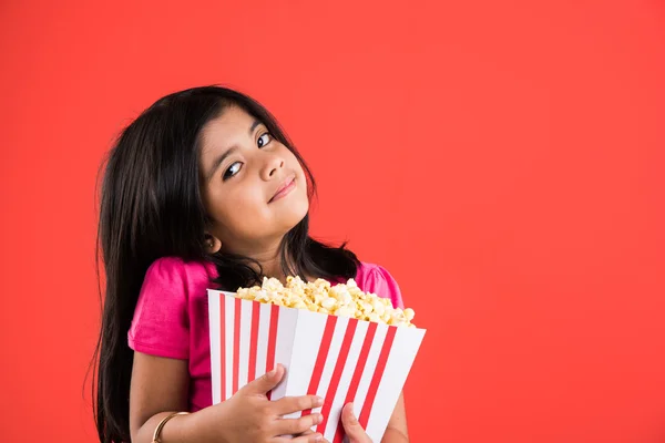 Fille heureuse manger du pop-corn et porter des lunettes, fille indienne manger du pop-corn, fille asiatique et pop-corn, petite fille manger du pop-corn sur fond rouge — Photo