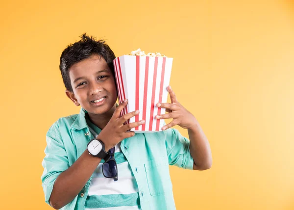 Fröhliches indisches Kind hält eine große Schachtel Popcorn in der Hand und blickt isoliert in die Kamera auf gelbem Hintergrund, Porträt eines entzückenden indischen Jungen, der Popcorn, asiatisches Kind und Popcorn isst — Stockfoto