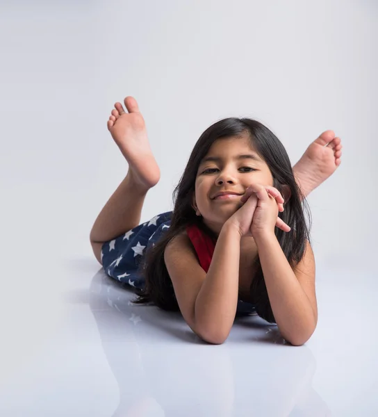 Indienne mignonne fille couchée sur le sol reposant sa tête dans ses mains, asiatique Petite fille riant, couchée sur le ventre, isolé sur fond blanc — Photo