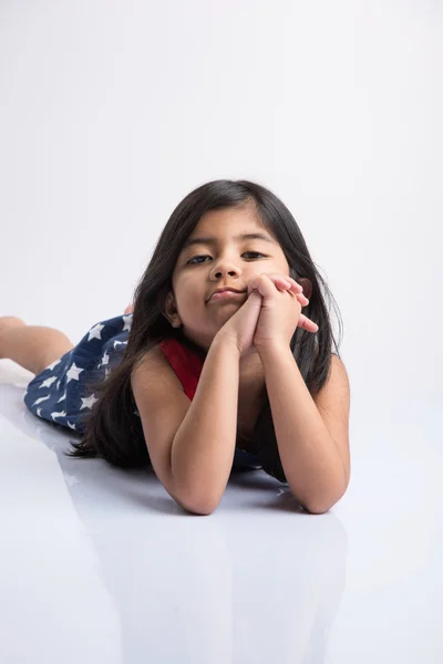 Indienne mignonne fille couchée sur le sol reposant sa tête dans ses mains, asiatique Petite fille riant, couchée sur le ventre, isolé sur fond blanc — Photo