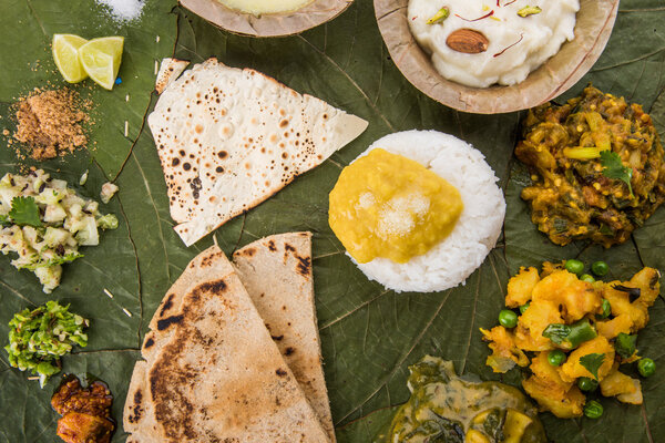 typical maharashtrian food served in plate and bowls made of leaf includes kadhi and shrikhand, plain dal, spinach curry, aalu mutter, plain rice, papad, bhakri or bhakar or roti and variety of salad