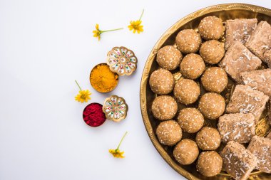 sesame laddu or tulgul or til gul laddu or ladu in brass plate with huldi and kumkum, indian traditional festival in january, indian sweet food, indian rituals, tilgul cake or vadi clipart