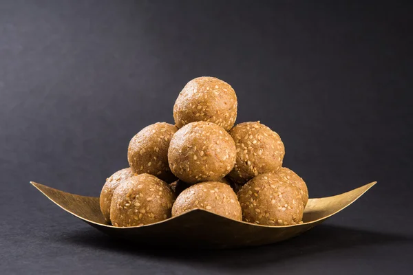 The indian sesame sweet or tilgul laddu, made up of jaggery and sesame seeds, indian sweet for Makar Sankranti festival, in terracotta bowl with jaggery & raw sesame