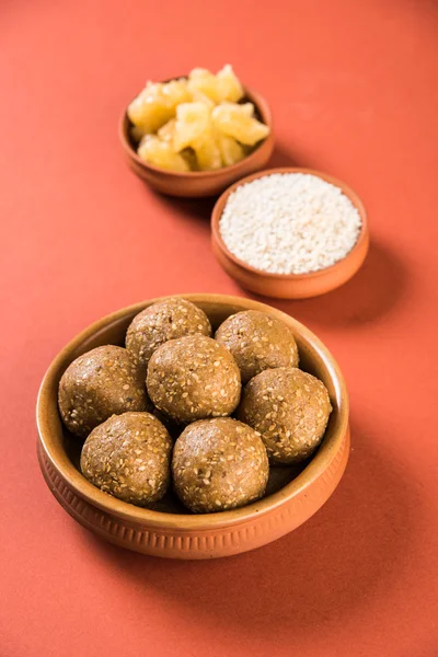 The indian sesame sweet or tilgul laddu, made up of jaggery and sesame seeds, indian sweet for Makar Sankranti festival, in terracotta bowl with jaggery & raw sesame — Stock Photo, Image