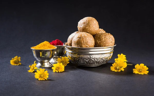 sesame laddu or tulgul or til gul laddu or ladu in brass plate with huldi and kumkum, indian traditional festival in january, indian sweet food, indian rituals, tilgul cake or vadi