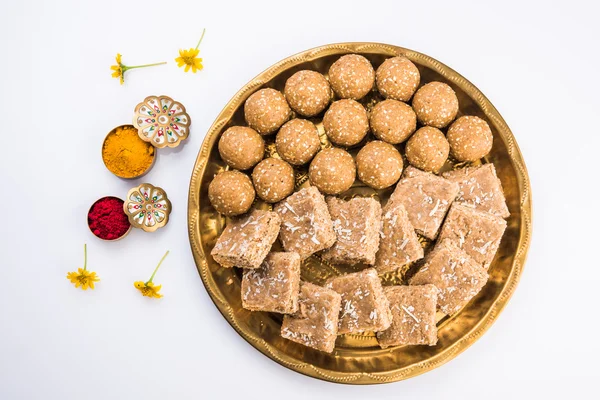 sesame laddu or tulgul or til gul laddu or ladu in brass plate with huldi and kumkum, indian traditional festival in january, indian sweet food, indian rituals, tilgul cake or vadi