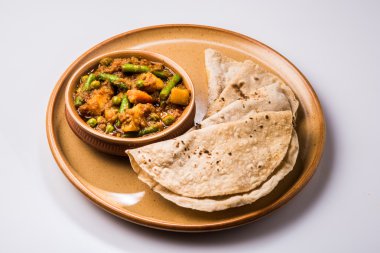 hint tarifi, geleneksel masala ve köri ile patates ve fasulye içeren karışık sebze, kırmızı sıcak ve baharatlı geleneksel chapati / fulka / hint roti / seramik plaka izole hint ekmeği ile servis