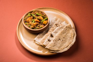 hint tarifi, geleneksel masala ve köri ile patates ve fasulye içeren karışık sebze, kırmızı sıcak ve baharatlı geleneksel chapati / fulka / hint roti / seramik plaka izole hint ekmeği ile servis