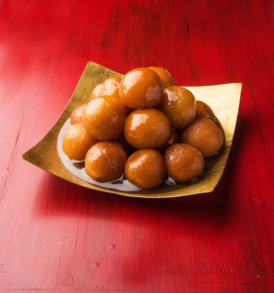 Gulab Jamun servido en un plato de latón cuadrado con jarabe dulce verter - Un plato dulce indio, de forma redonda, negro o marrón textura servida como postre, altas calorías, comida diwali — Foto de Stock