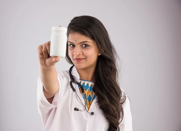 Indisk kvinnlig läkare som håller upp en vit flaska tabletter, Asiatisk kvinnlig läkare som visar vita piller flaska, lämplig för reklam, isolerad på grå bakgrund — Stockfoto
