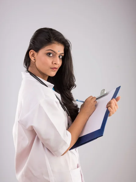 Ung söt indian kvinnlig läkare med hälsokort eller skrivblock, asiatisk kvinna och skrivblock, isolerad på grå bakgrund — Stockfoto