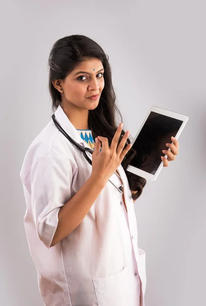 Vacker kvinnlig indisk läkare tittar på en digital tablett & klädd i en vit kappa plus stetoskop — Stockfoto