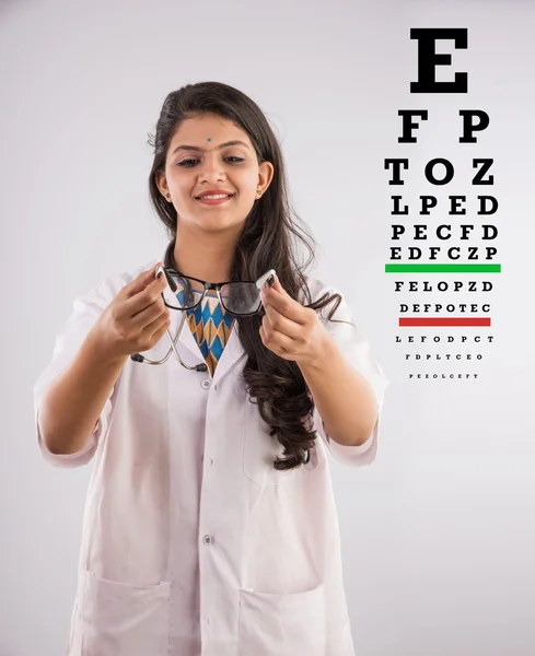An Indian female nurse with a specs or spectacle or eye wear and eye test chart in the background, isolated on gray background