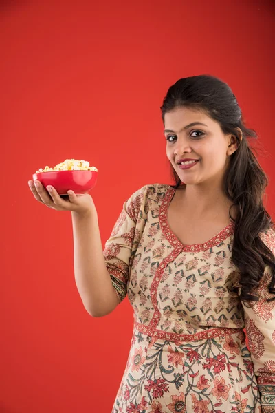 Indiase jong en mooi meisje eten popcorn, Aziatisch meisje geniet popcorn of pop corn, geïsoleerd op rode achtergrond — Stockfoto