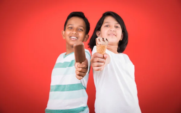 Two happy indian kids and ice cream, two asian kids enjoying ice cream or cone or chocolate candy, girl and boy eating ice cream, isolated on red background, — Stock Photo, Image