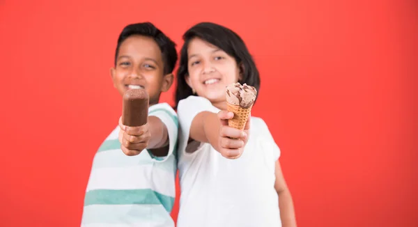 Two happy indian kids and ice cream, two asian kids enjoying ice cream or cone or chocolate candy, girl and boy eating ice cream, isolated on red background, — Stock Photo, Image