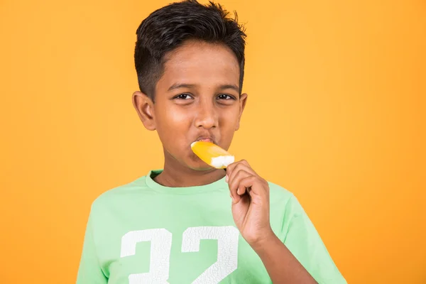 Kleiner indischer Junge isst Eislutscher oder Eisbonbons, indischer Junge isst Mango-Eis, asiatischer Junge und orangefarbene Eisbonbons, isoliert auf gelbem Hintergrund, 10-jähriger Junge und Eis — Stockfoto